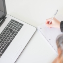 woman writing a list by a laptop