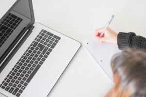 woman writing a list by a laptop